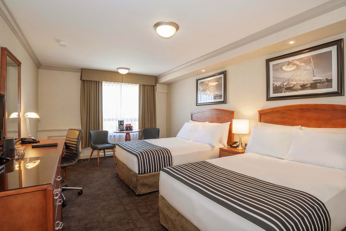 Une chambre d’hôtel avec deux lits, un bureau, une chaise, une table basse et une grande fenêtre avec des rideaux.