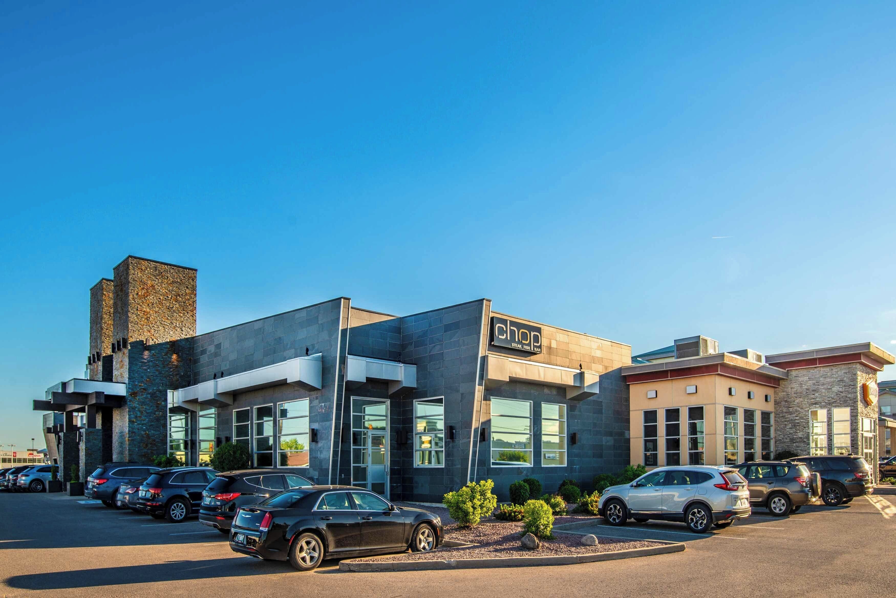 A modern building with a stone facade, large windows, and a parking lot with several cars.