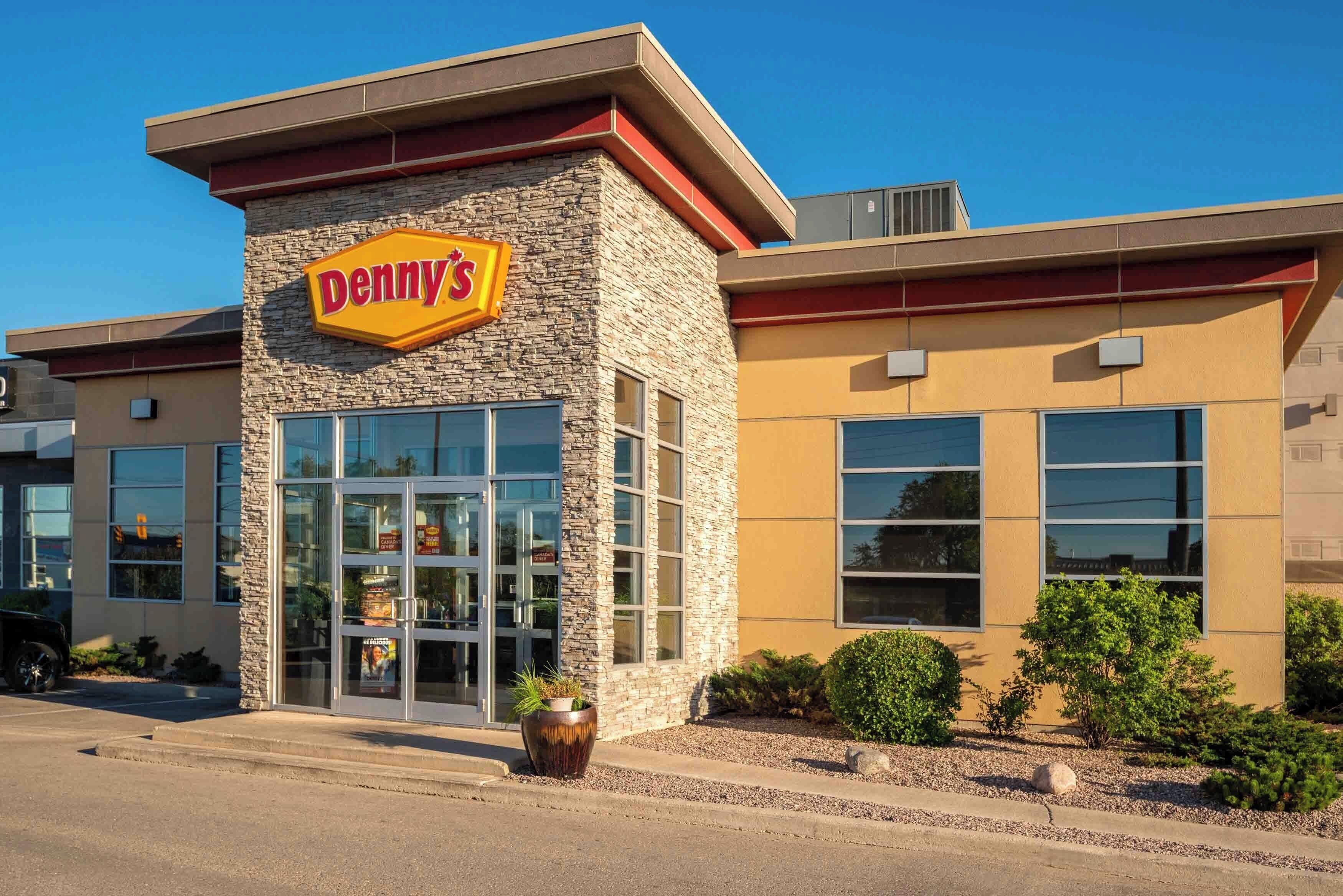 A Denny's restaurant with a stone facade, large windows, and a clear sky.