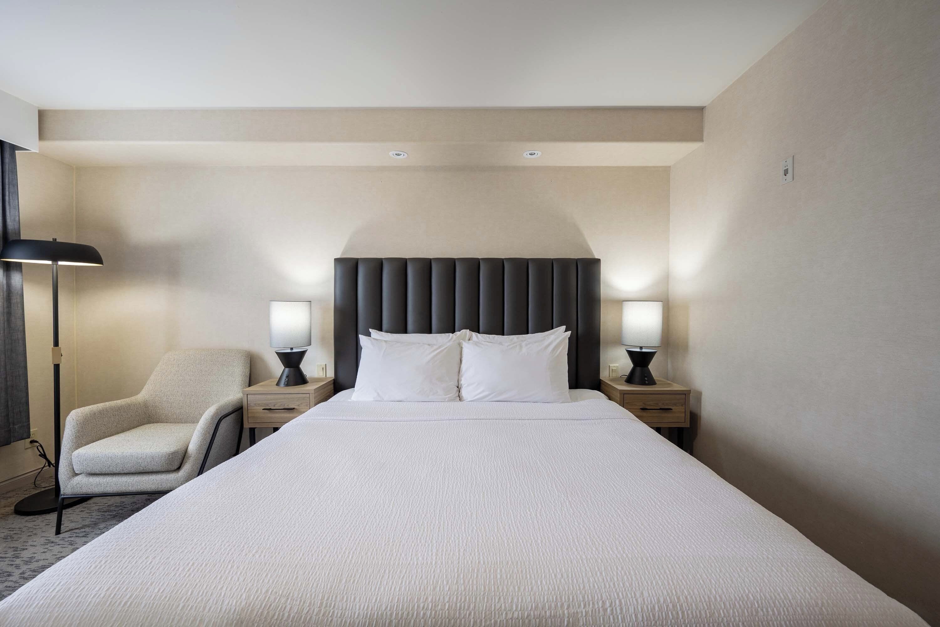 Ett hotellrum med en stor säng, två sängbord med lampor, en stol och en modern sänggavel.