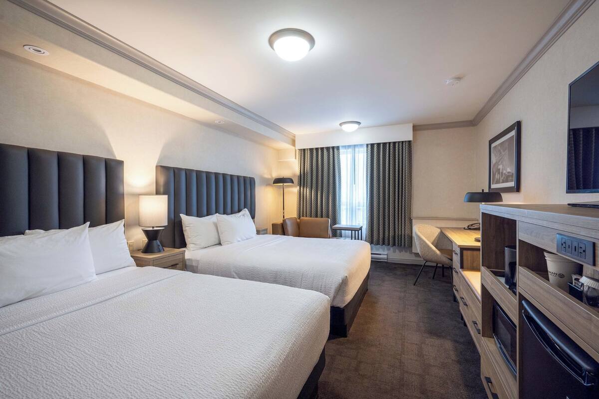 Une chambre d’hôtel avec deux lits, un bureau, une chaise, une télévision et une kitchenette.