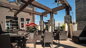 Ein möblierter Patio-Bereich im Freien mit Korbmöbeln, Steinpfeilern und Deckenventilatoren.