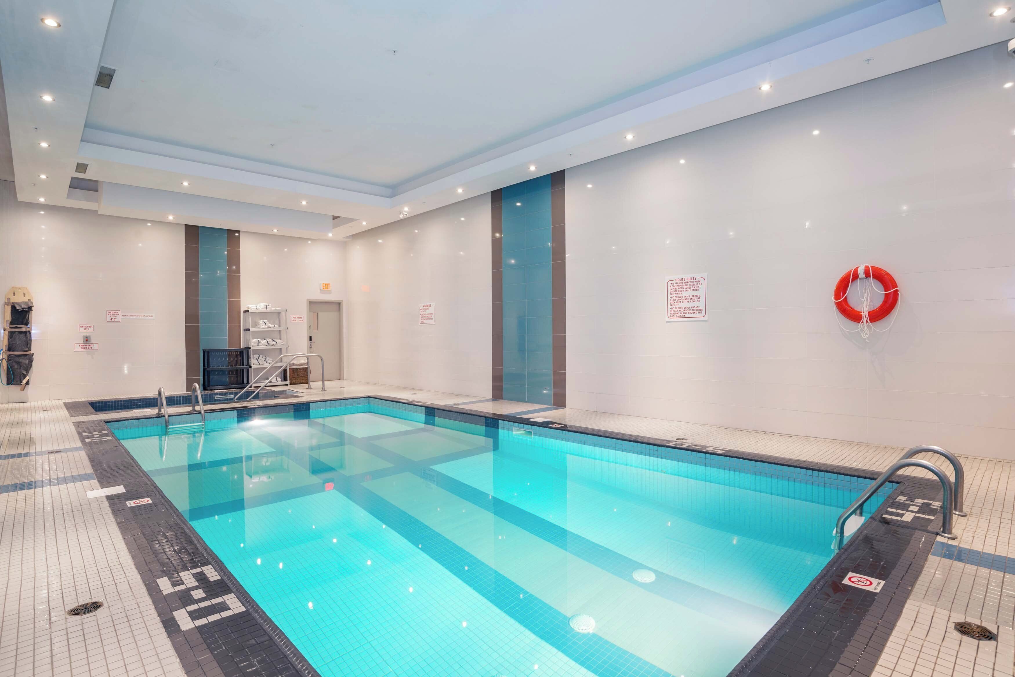 Une piscine intérieure à l’eau claire, avec des murs carrelés et une bouée de sauvetage placée à droite.