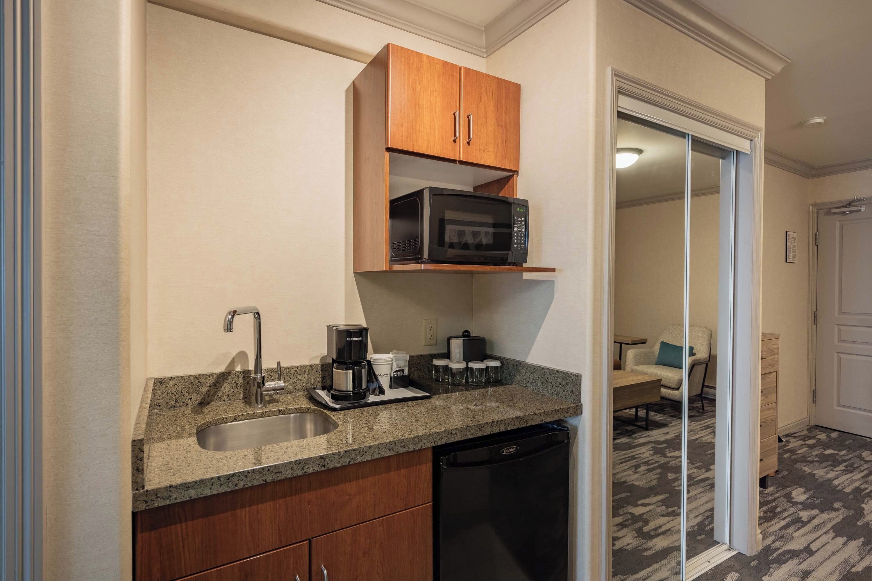 A compact kitchen with a granite countertop, a built-in microwave, a coffee maker, and a dishwasher.