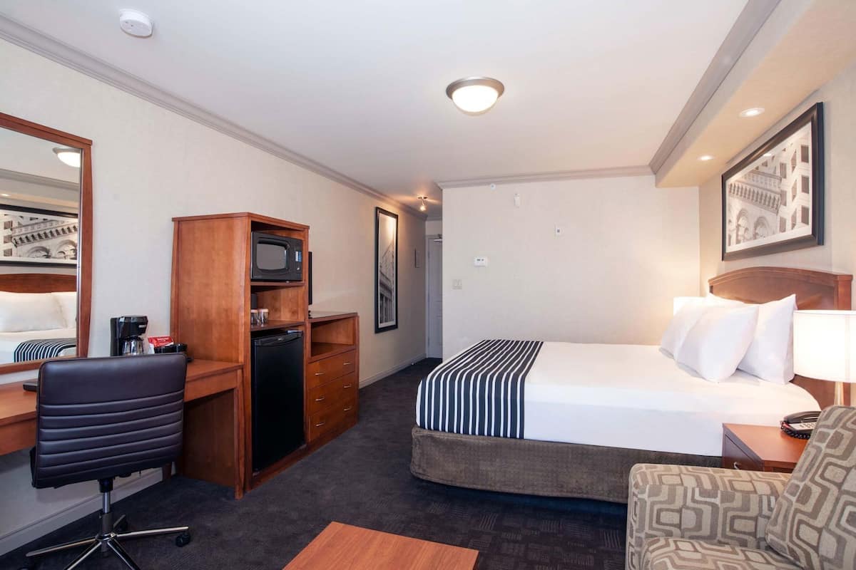 A hotel room with a bed, desk, chair, microwave, and refrigerator.