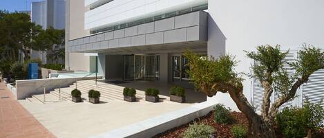 A modern building with a flat facade, large windows, and a landscaped area with trees and shrubs.