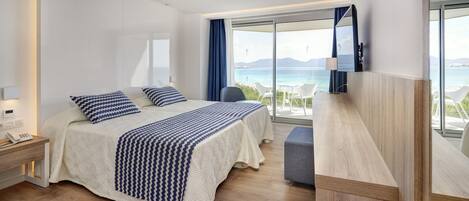 A hotel room with a large bed, a bedside phone, a desk, and a view of the sea.