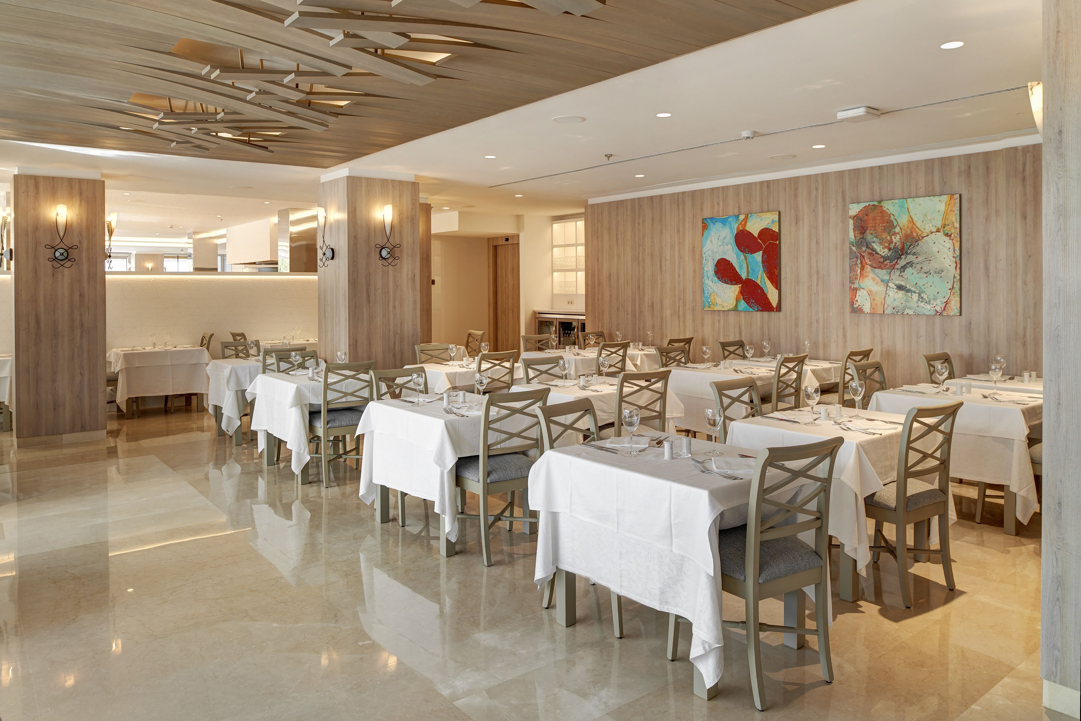A spacious dining area with multiple tables and chairs, wooden paneling on the walls, and modern ceiling design.