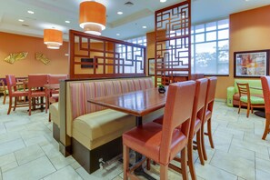 Un restaurant avec des banquettes, des tables hautes et des chaises. Les murs sont décorés de panneaux et il y a une grande fenêtre.