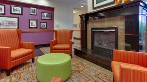 A lobby with striped orange chairs, a green ottoman, and a fireplace.