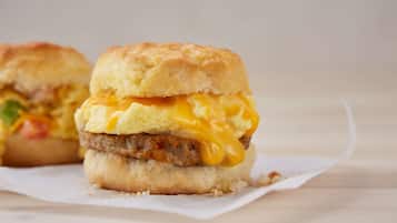 Un sándwich de desayuno con un panecillo, huevo, queso y una hamburguesa de carne.