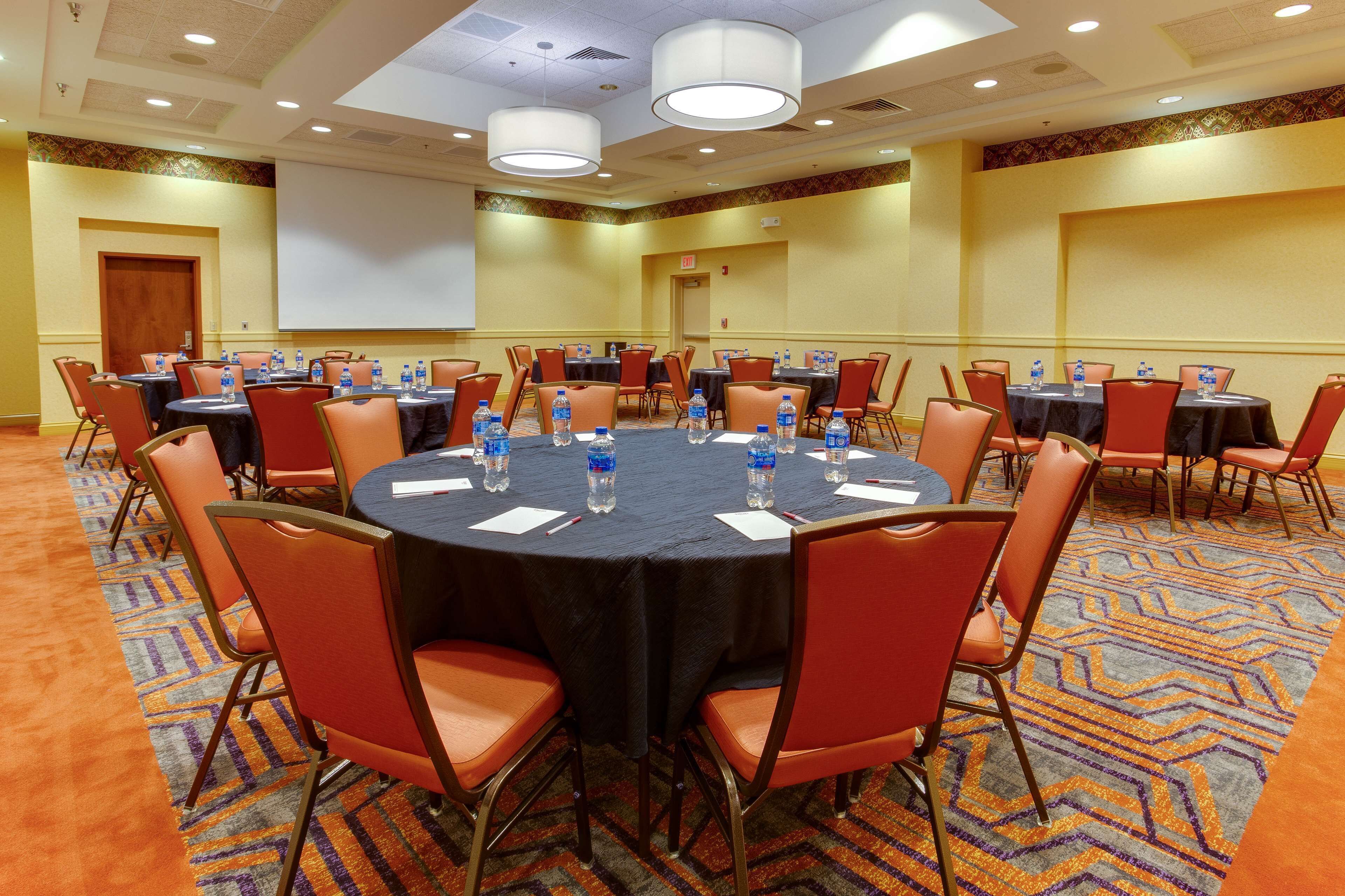 A conference room with round tables, orange chairs, and water bottles.
