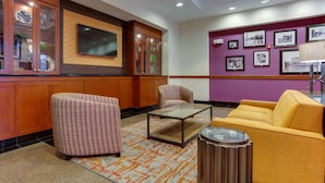 A lobby with a checkered armchair, a yellow sofa, a glass-top coffee table, and a cabinet with glass doors.