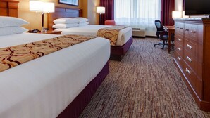 A hotel room with two beds, a desk, a television, and a dresser.