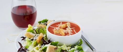 A white plate with a salad and a bowl of tomato soup garnished with croutons and cheese.