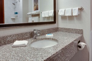 Un baño con lavamanos de encimera de granito, un espejo y un perchero con tres toallas.