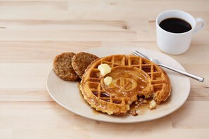A plate with waffles, syrup, and butter, and a cup of coffee on a wooden table. - Drury Inn & Suites West Des Moines (West Des Moines)