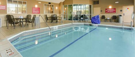 An indoor swimming pool with clear lane markings, a lifeguard station, and a seating area with tables and chairs.