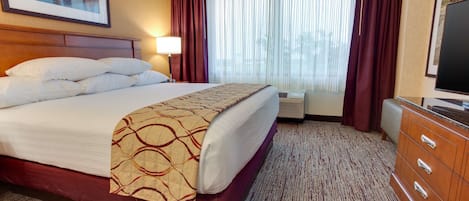 A hotel room with a large bed, a dresser, a television, and a window with curtains.