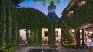 Une cour avec une fontaine, un chemin de pierre et un espace aménagé avec des sièges, le tout entouré de verdure.