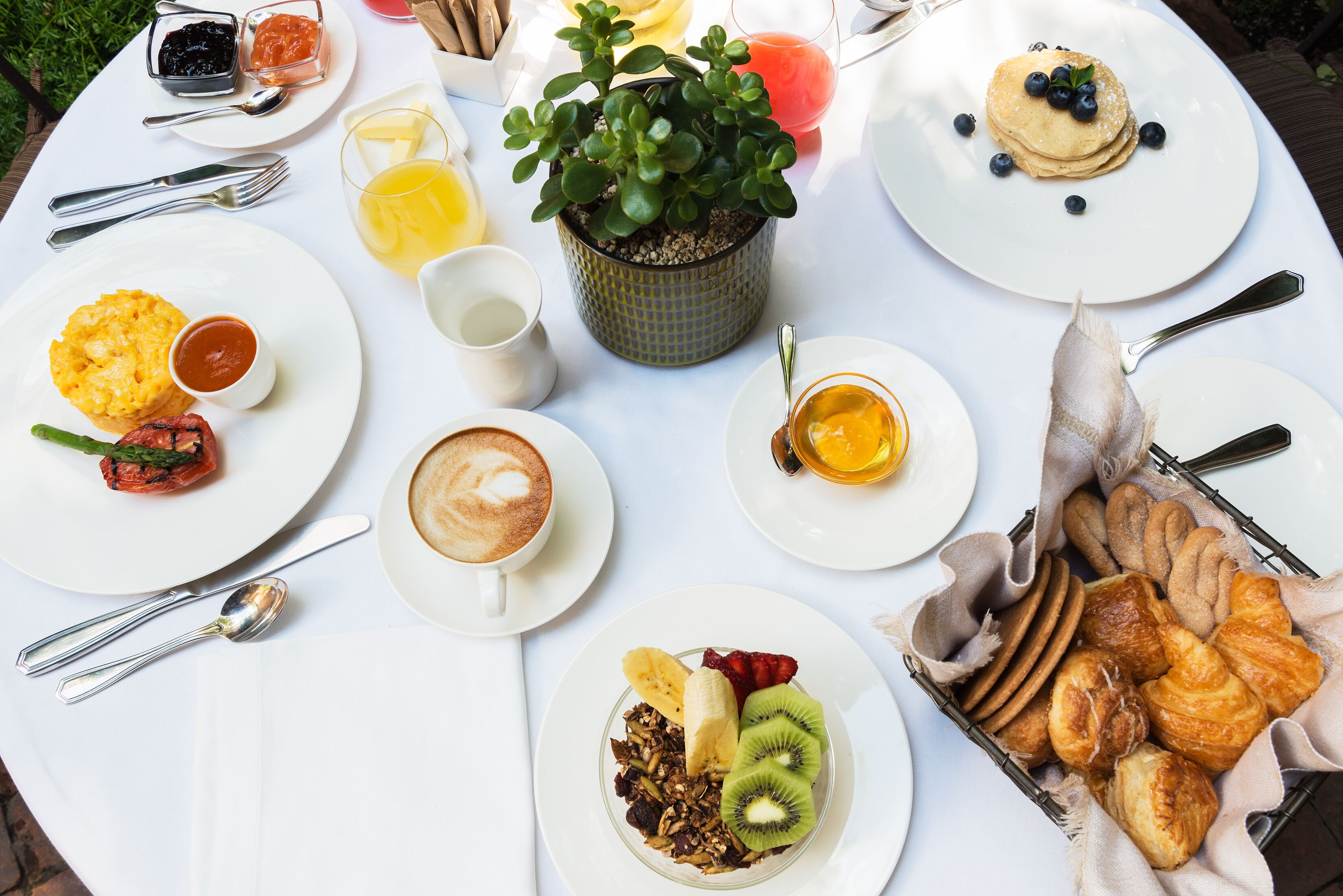Mesa de café da manhã com diversos pratos, incluindo panquecas, frutas, doces e uma xícara de café.