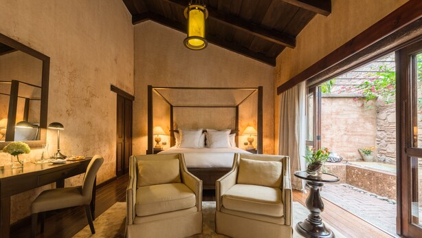 Een slaapkamer met een hemelbed, twee fauteuils, een bureau en een nachtkastje.