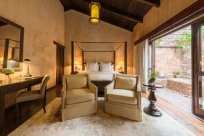 A bedroom with a four-poster bed, two armchairs, a desk, and a nightstand.