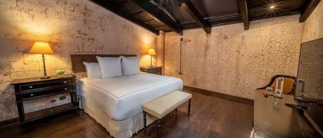 Quarto com cama, mesas de cabeceira, um banquinho e um guarda-roupa.