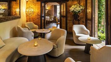 A cozy lounge area with comfortable seating, small round tables, and a brick wall backdrop.