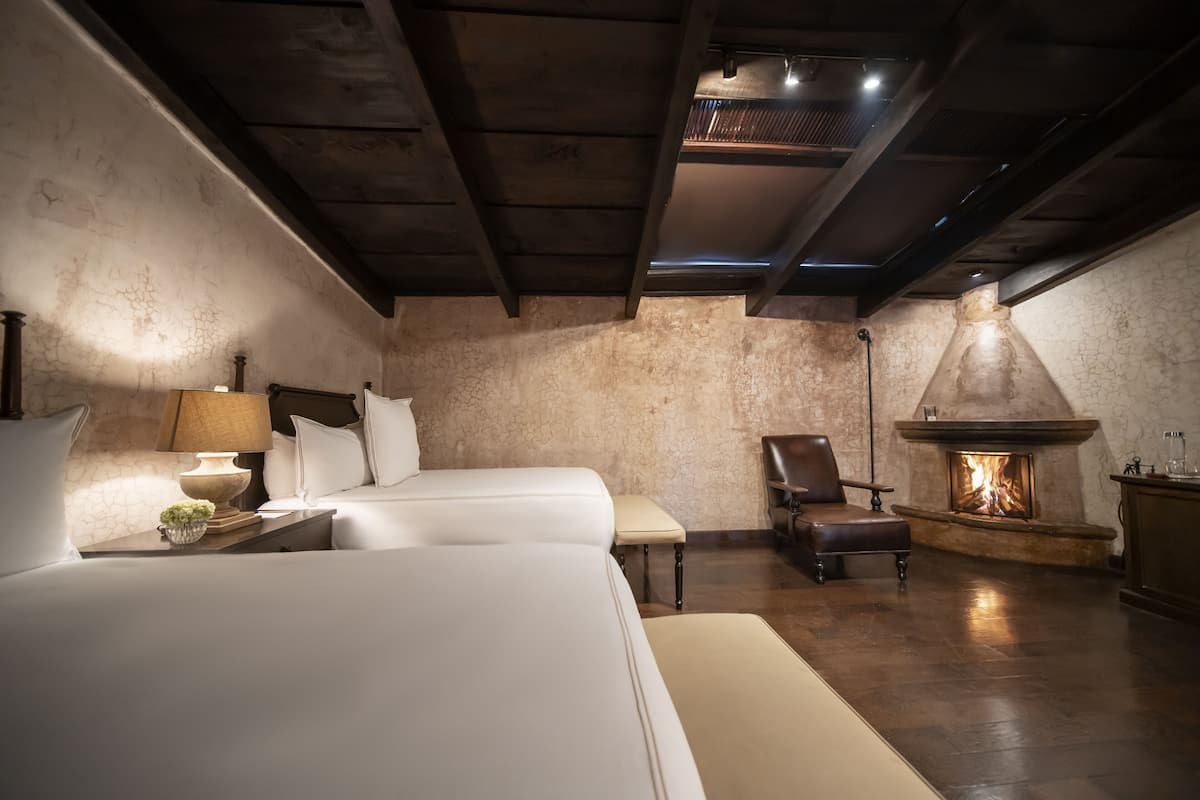 Un dormitorio acogedor con dos camas, una chimenea y una mesita de noche con lámpara.