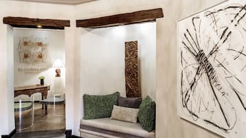 A lobby with a sofa, a table, and chairs, a decorative wall piece, and a sign for 'EL CONVENIENTE BOUTIQUE HOTEL'.