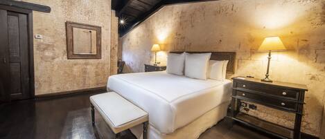 Un dormitorio con una cama grande, mesitas de noche con lámparas, un banco y techo de madera.