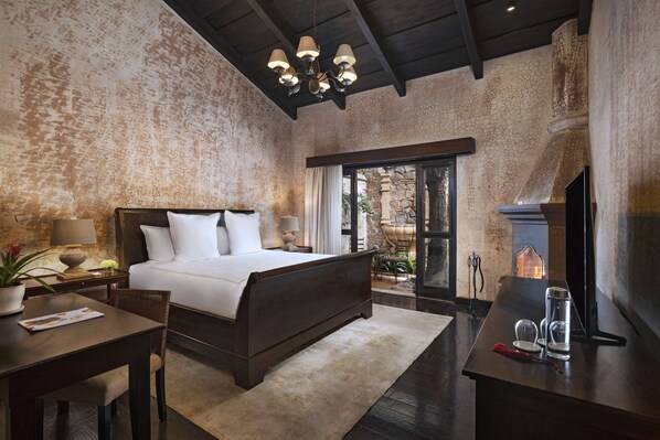 A bedroom with a large bed, a desk, a chair, a fireplace, and a view of the outdoors.