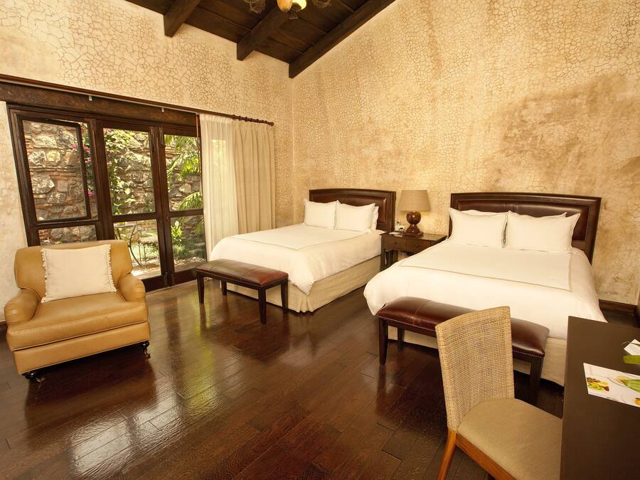Habitación de hotel con dos camas, un sofá, una silla, un escritorio y una ventana con cortinas.