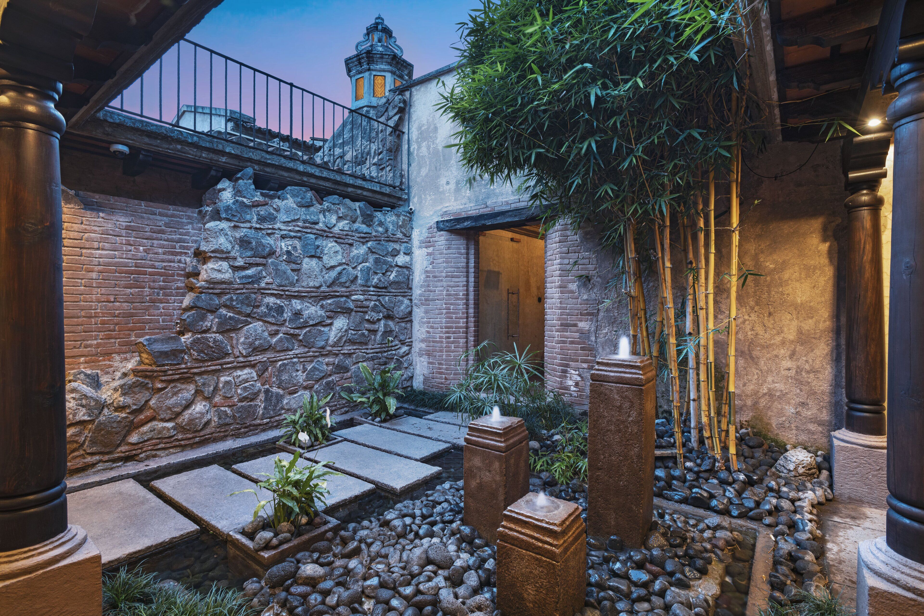 A courtyard with stone walls, bamboo plants, and a stone pathway.