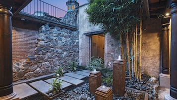 A courtyard with stone walls, bamboo plants, and a stone pathway.