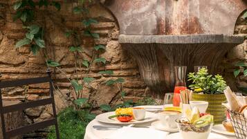 A table set with a variety of dishes, a chair, and a decorative stone wall with a fountain.