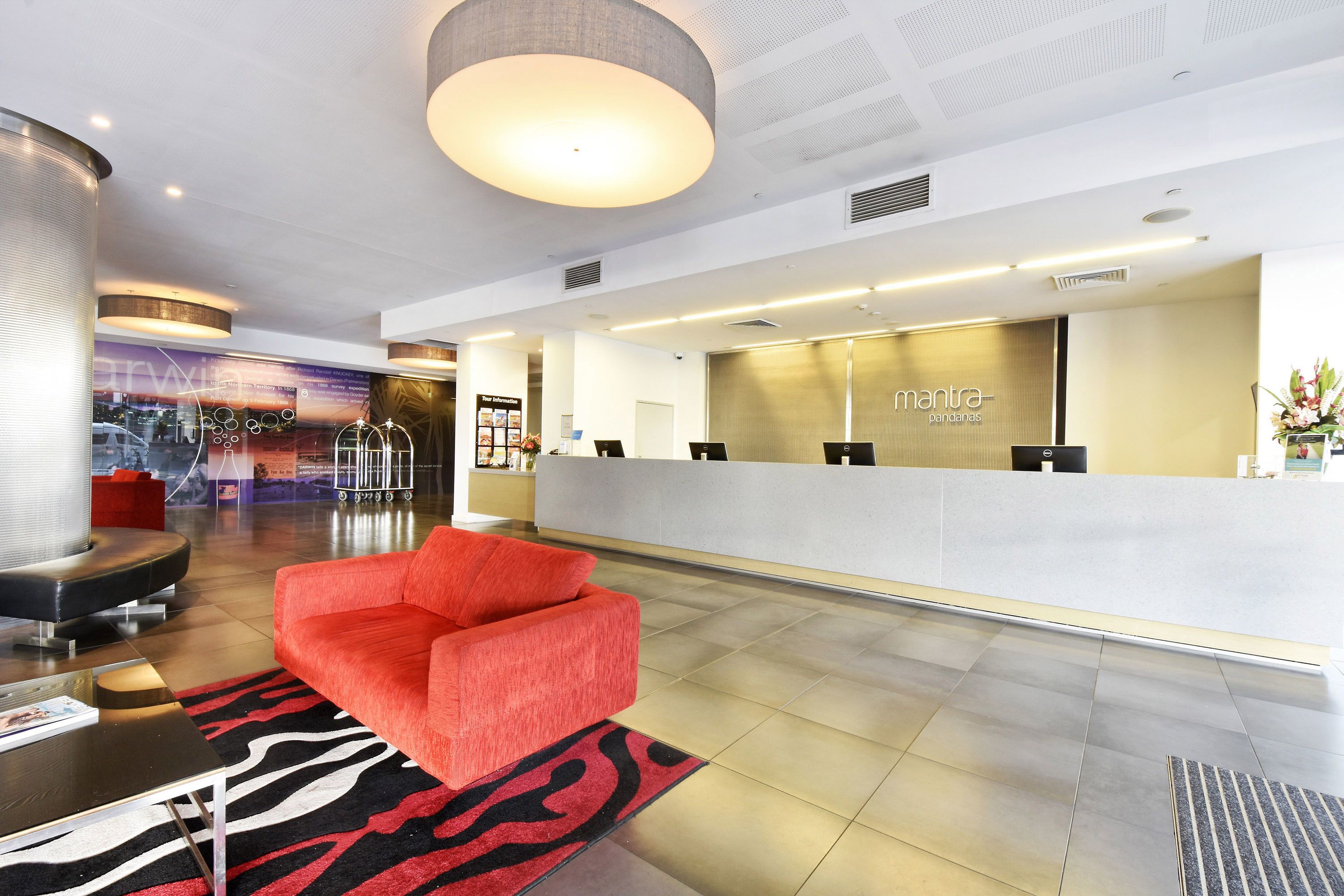 Un hall d’hôtel moderne avec un comptoir d’accueil, un canapé rouge et un tapis à motifs.