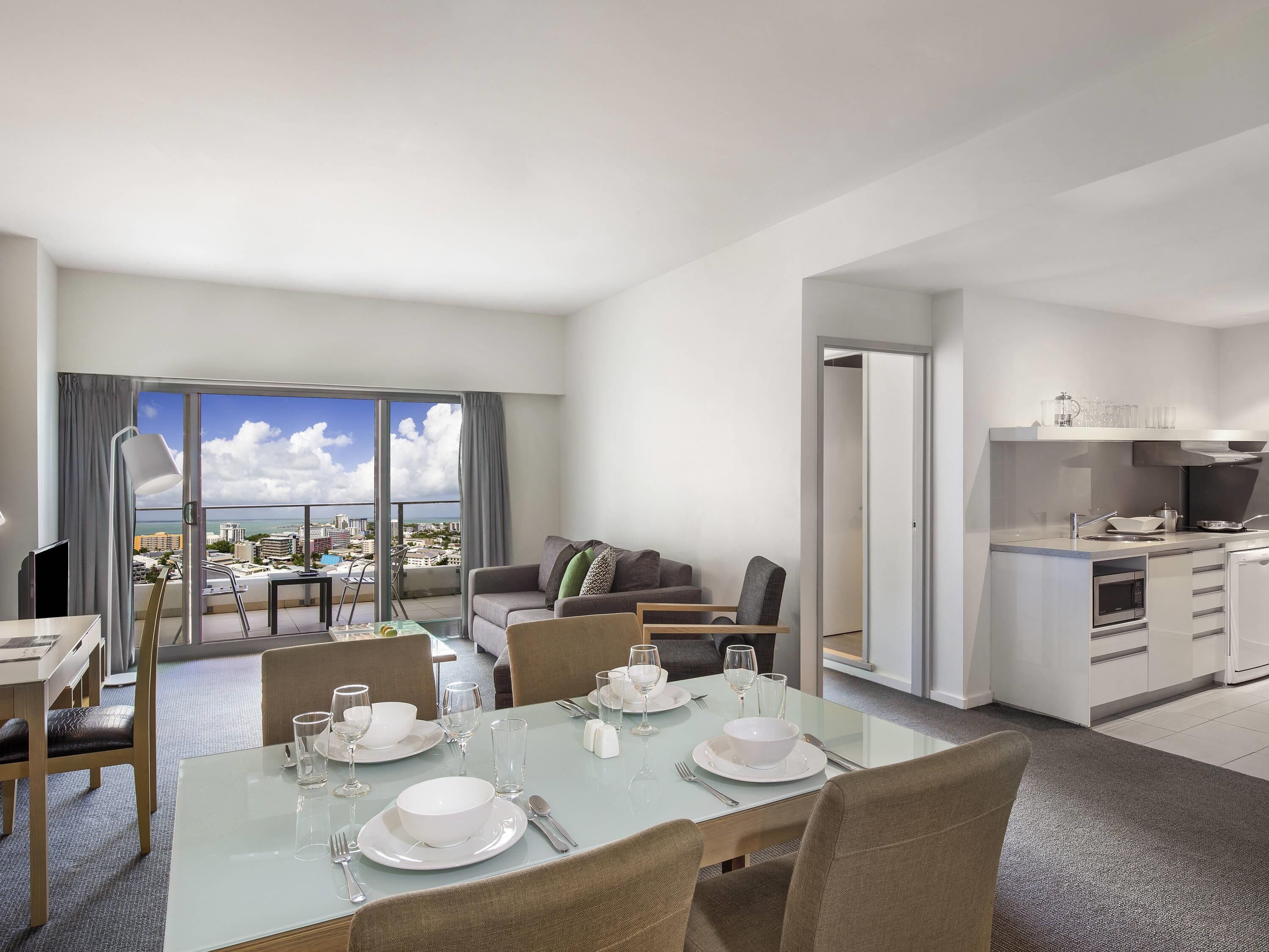 A modern hotel room with a dining area, a living room with a view, and a kitchenette.