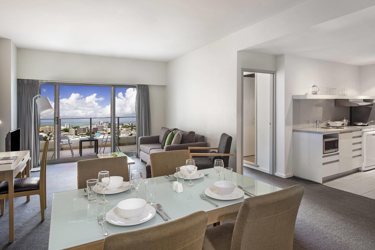 A modern hotel room with a dining area, a living room with a view, and a kitchenette.
