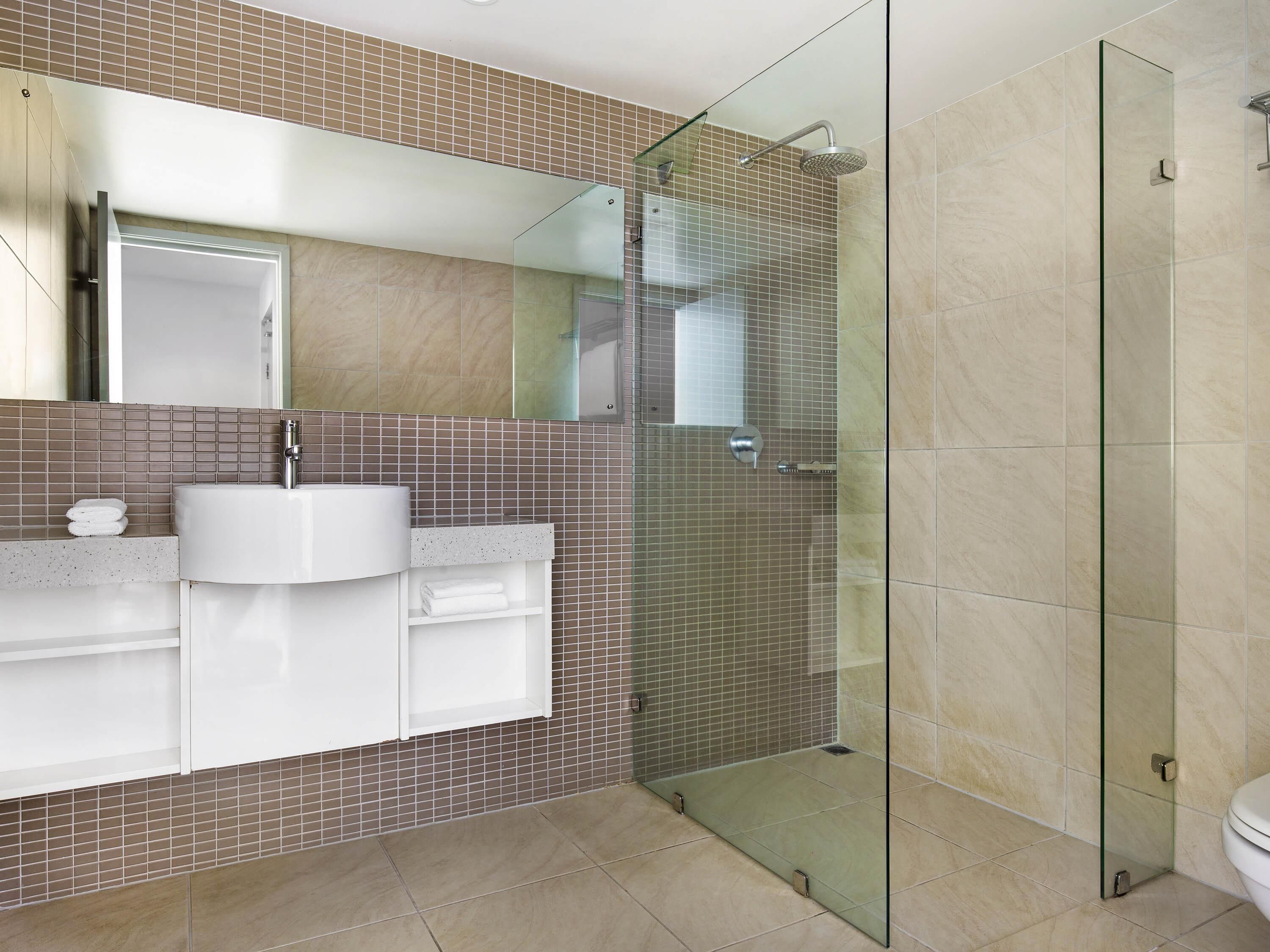 A modern bathroom with a glass-enclosed shower, a white sink, and a tiled backsplash.