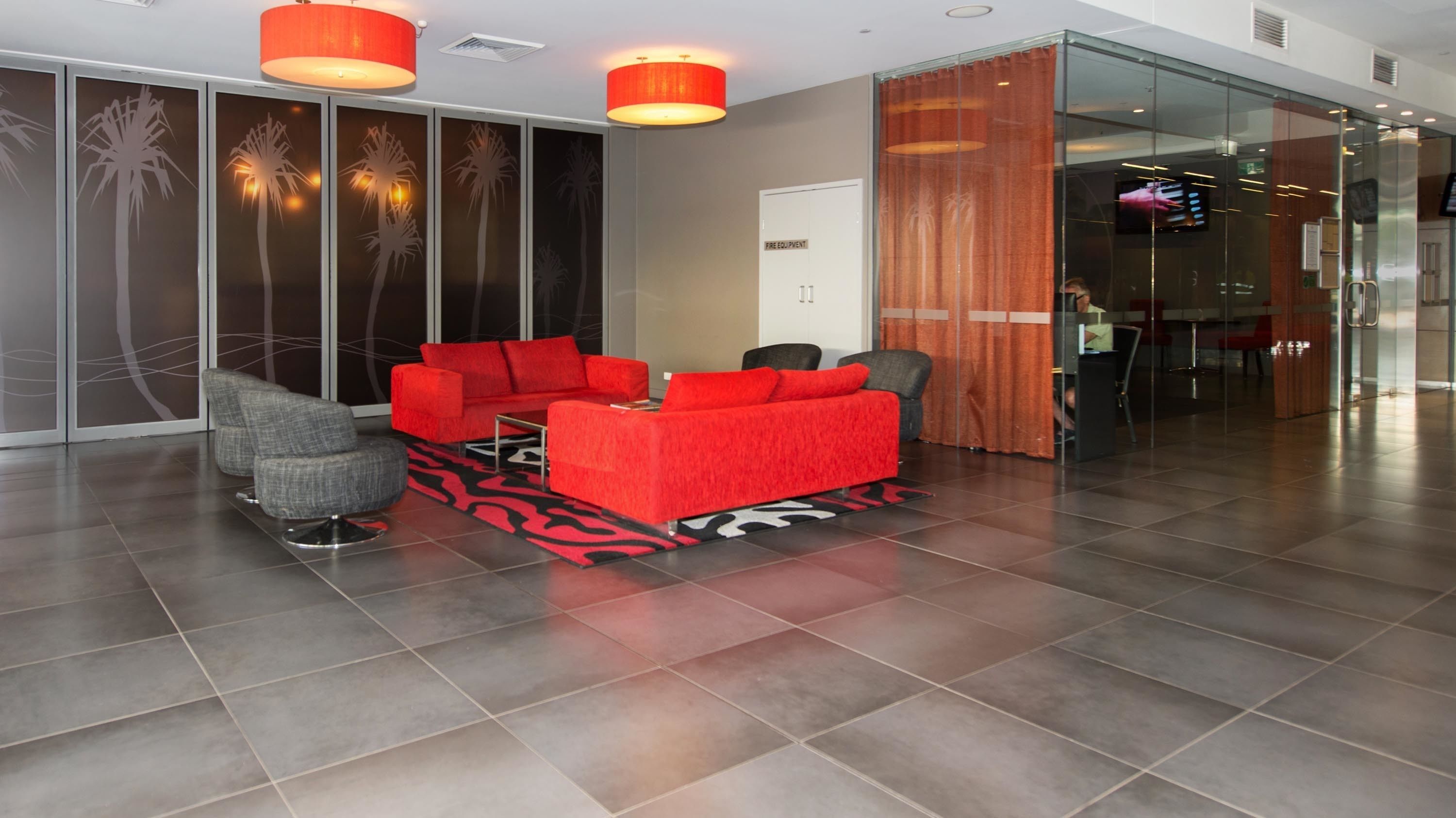 A modern lobby with a red sofa set, a grey armchair, and a patterned rug.