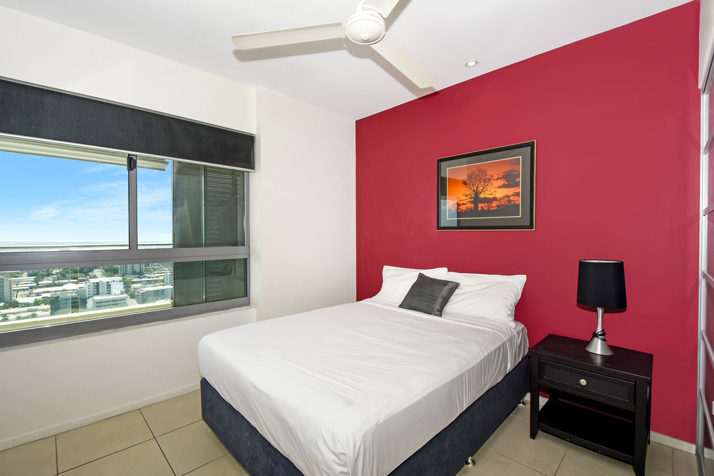 A bedroom with a bed, a nightstand, a ceiling fan, a window with blinds, and a red wall.