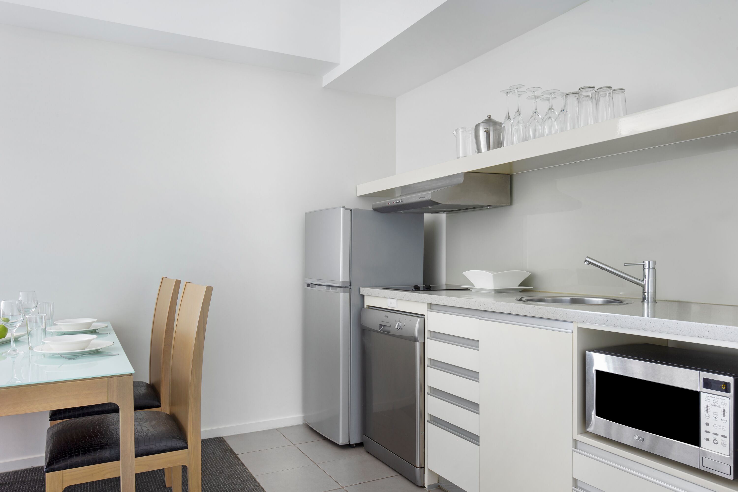 A modern kitchen with a dishwasher, refrigerator, microwave, and a dining area with a table and chairs.