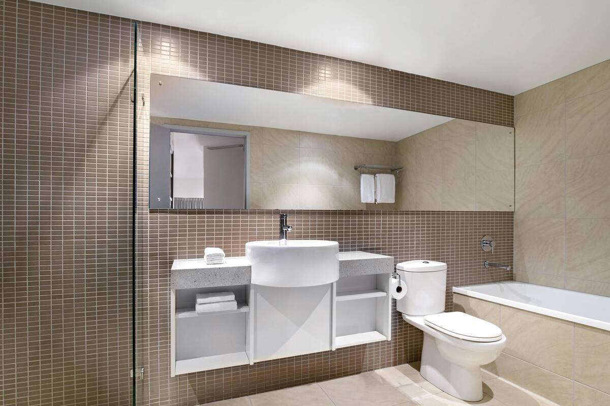 A bathroom with a sink, toilet, and bathtub, featuring tiled walls and a mirror above the sink.