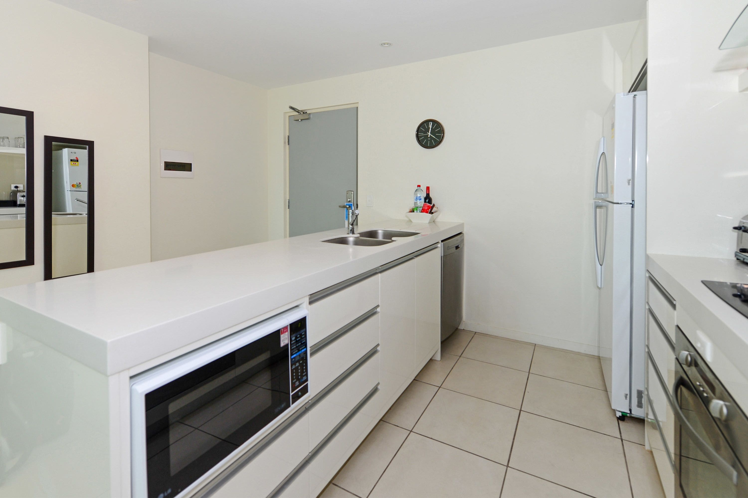 A modern kitchen with white cabinetry, a built-in oven, a sink, and a refrigerator.