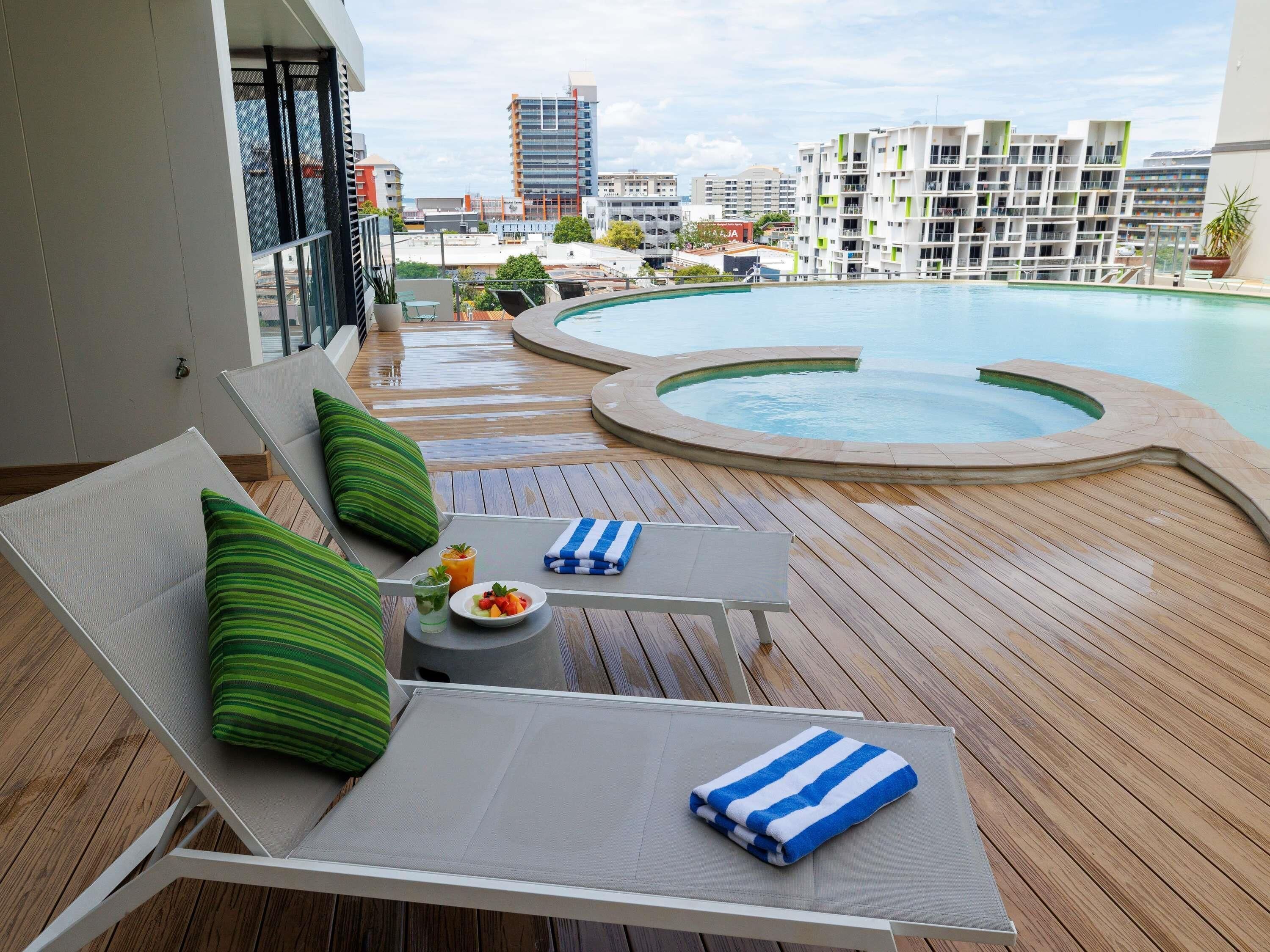 A poolside area with lounge chairs, a small table with a drink and fruit, and a view of the cityscape.