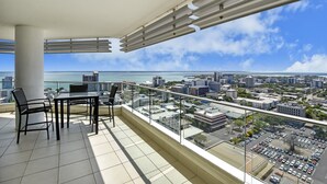 A balcony with a table and chairs, offering a city view and a glimpse of the sea. - Mantra Pandanas (Darwin)