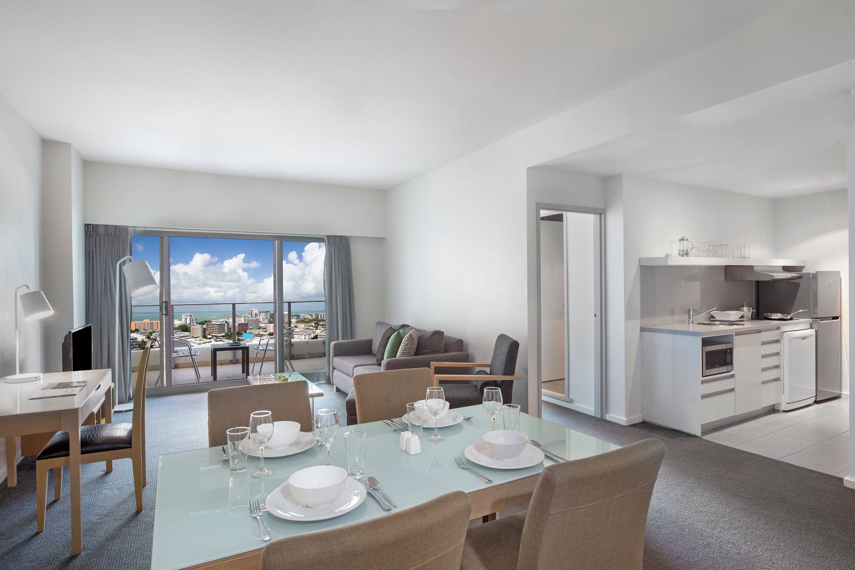 Ein modernes Hotelzimmer mit Essbereich, einer Küche und einem Balkon mit Blick auf die Stadt.