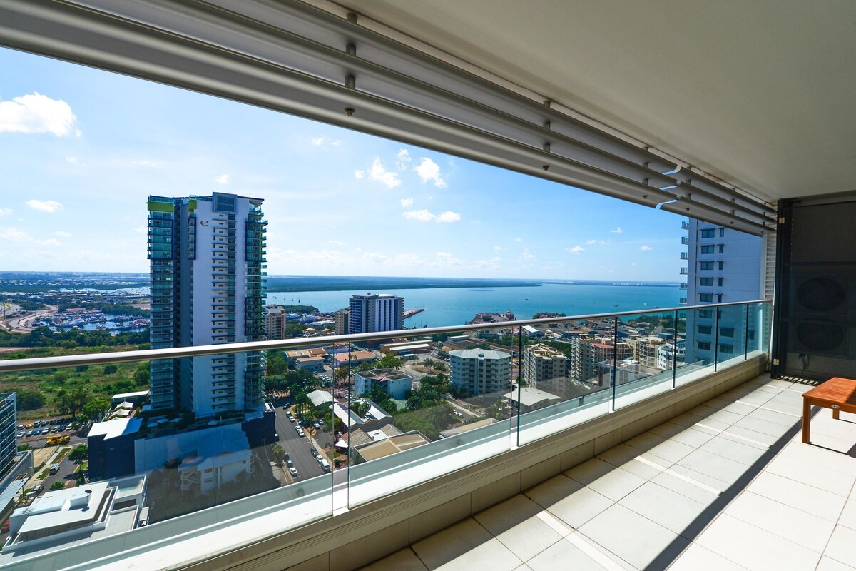 A balcony with a glass railing overlooking a cityscape and a body of water.